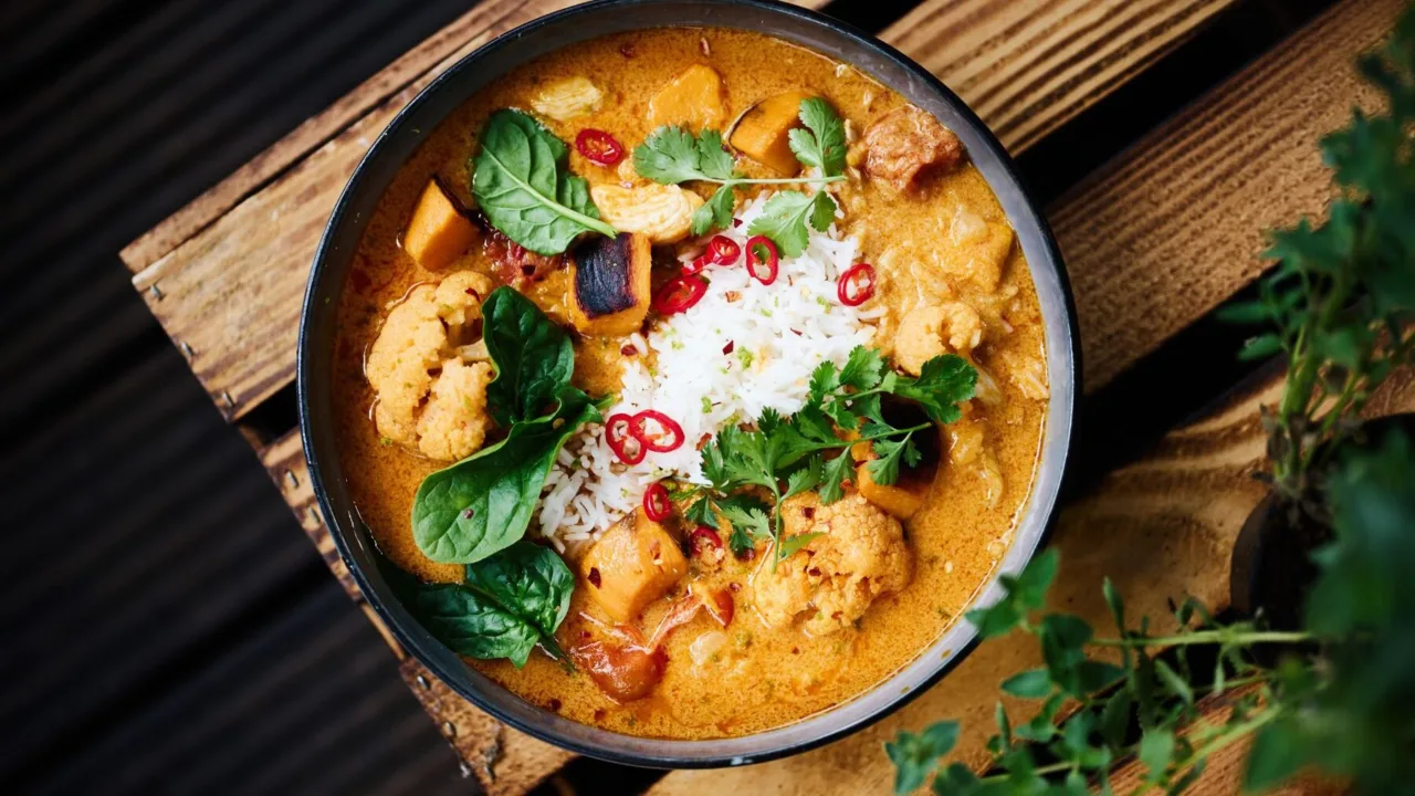 Krémes zöldséges curry rizzsel, chilivel és friss bazsalikommal egy sötét tálban.